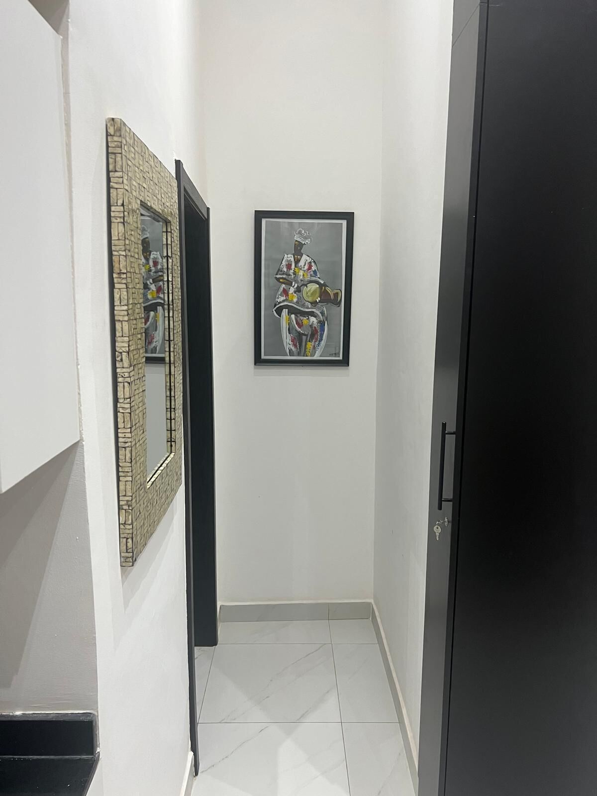 A hallway with a tiled floor, a door on the right, and two framed artworks on the walls.