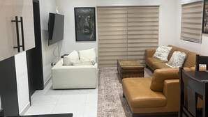Una sala de estar moderna con un sofá blanco, un sofá de cuero marrón, un televisor y un ventanal con persianas.