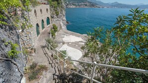 Vista costera con una escalera de piedra que baja a una playa, con vista al mar y montañas distantes.