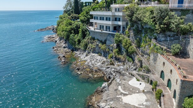 Un edificio costero con fachada de piedra, un balcón y vista al mar.