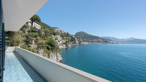 Un balcón con vistas a un pueblo costero, mar azul cristalino y montañas a lo lejos.