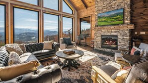 A spacious living room with large windows, a stone fireplace, and a comfortable seating area. - Ridgetop Retreat, Sleeps 11・Theater・Pool・Hot tub (Sevierville)