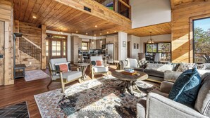 A spacious living area with a high ceiling, wooden beams, a large rug, and a dining area with a table and chairs. - Ridgetop Retreat, Sleeps 11・Theater・Pool・Hot tub (Sevierville)