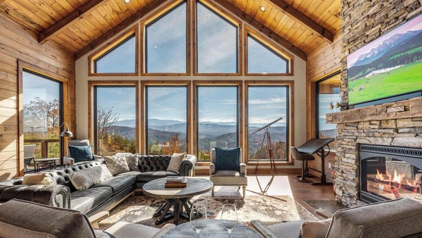 A spacious living room with a large fireplace, comfortable seating, and a scenic mountain view through large windows. - Ridgetop Retreat, Sleeps 11・Theater・Pool・Hot tub (Sevierville)