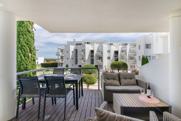 Ein Balkon mit Esstisch, Stühlen und einer Couch. Blick auf ein Gebäude mit Balkonen und einer begrünten Wand.