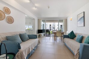 A modern living room with a sofa, a television, and a dining area with a table and chairs.