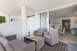 Ein modernes Wohnzimmer mit Rattanmöbeln, einem Holztisch und Blick auf die angrenzende Küche.