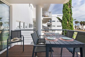 A balcony with a table set for two, chairs, and a hat on one chair. - Apartment 'Golden Sea' with Shared Pool, Wi-Fi and Air Conditioning (Cabanas de Tavira)