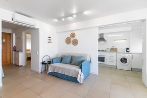 A modern kitchen with a washing machine, a dining area with a table and chairs, and a living area with a sofa and decorative wall hangings. - Apartment 'Golden Sea' with Shared Pool, Wi-Fi and Air Conditioning (Cabanas de Tavira)