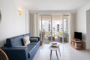 Un salon moderne comprenant un canapé, une table basse, un téléviseur posé sur un meuble en bois et une porte-fenêtre coulissante donnant sur un balcon extérieur.