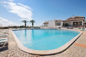 A swimming pool with lounge chairs, a building with a balcony, and palm trees in the background. - Apartment 'Golden Sun' with Shared Pool, Wi-Fi and Air Conditioning (Tavira)