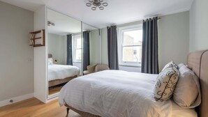 Une chambre avec un grand lit, un miroir, une chaise et une fenêtre avec des rideaux.