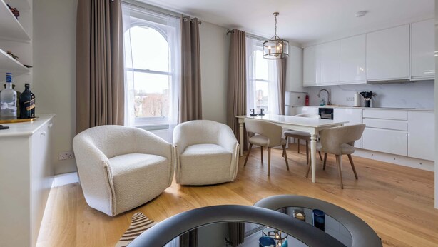 Une cuisine moderne avec des meubles blancs, une table à manger et deux fauteuils blancs.