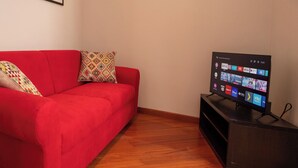 Ein rotes Sofa mit gemusterten Kissen, ein Flachbildfernseher auf einem Schrank und Holzboden.