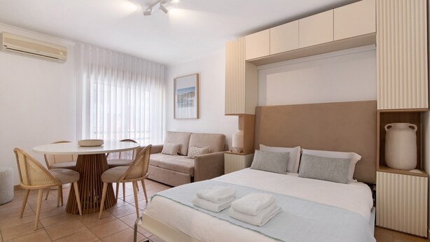 Ein Hotelzimmer mit einem Bett, einem runden Esstisch mit Stühlen, einer Couch, einer Nachttischlampe und einem an der Wand montierten Heizkörper.