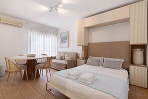 Une chambre d’hôtel comprenant un lit, une table de salle à manger ronde avec des chaises, un canapé, une lampe de chevet et un radiateur fixé au mur.