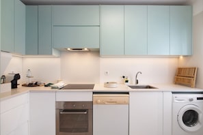 Une cuisine moderne avec des meubles blancs, un four encastré, un lave-vaisselle et un lave-linge.