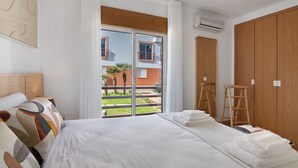 Ein Hotelzimmer mit Bett, einem Holzschrank, einem Balkon mit Blick auf Gebäude und einer Klimaanlage.
