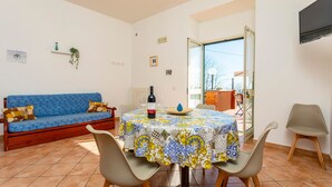 A dining area with a table set for two, a sofa, and a TV mounted on the wall.