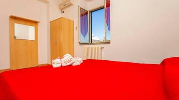 Une chambre avec un lit rouge, une armoire en bois et une fenêtre avec des rideaux.