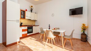 A modern kitchen with white cabinets, a dining table with chairs, a TV mounted on the wall, and a clock.