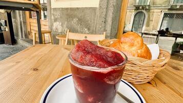 A table with a glass of red beverage, a white plate with a blue rim, and a basket with bread.