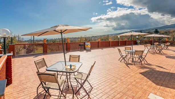 Un patio exterior con mesas, sillas, sombrillas y vistas al paisaje.