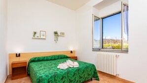 Un dormitorio con cama, mesita de noche, ventana y vistas, y un radiador.