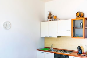 A compact kitchen with white cabinets, a gas stove, a sink, and a clock on the wall.