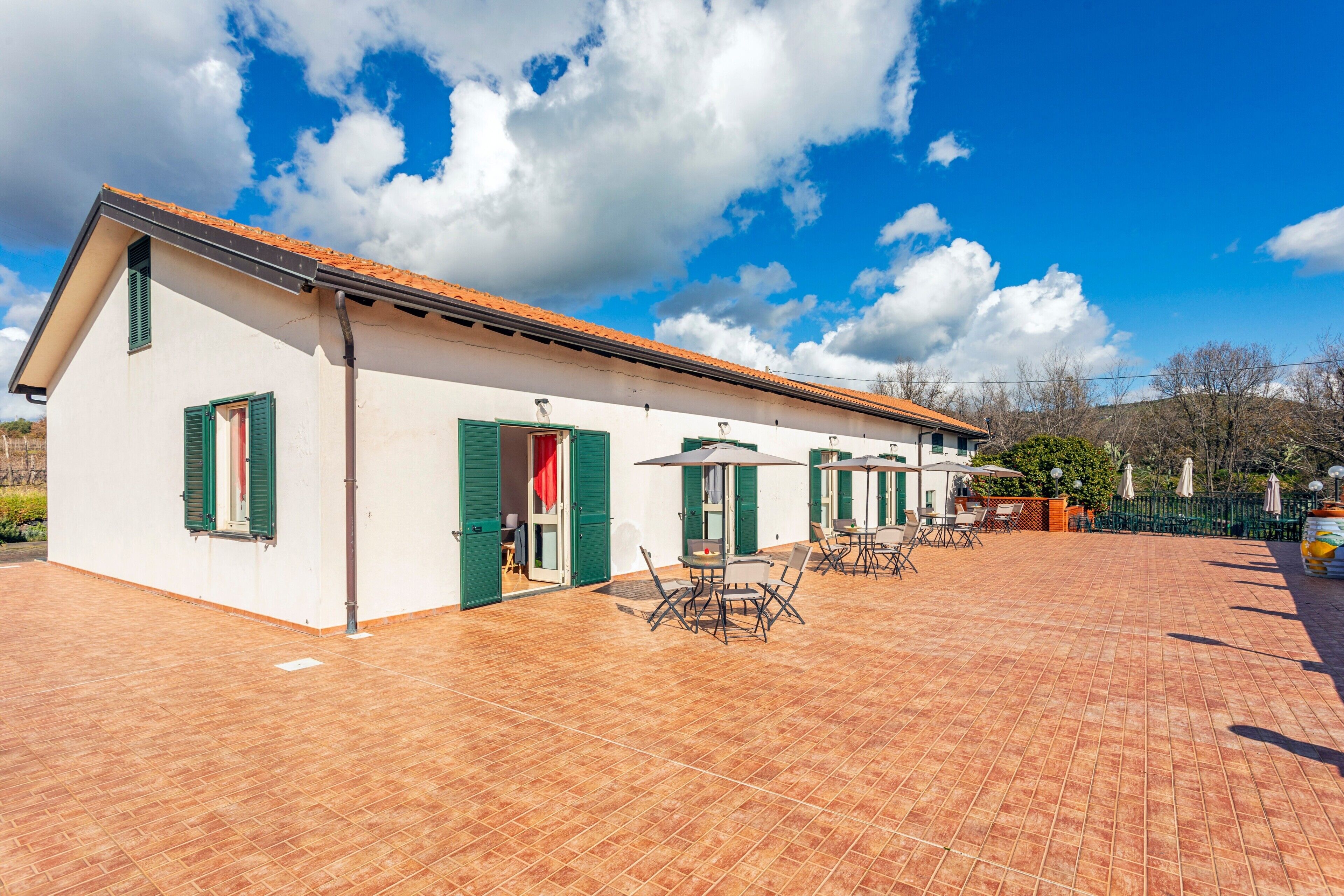 A building with a tiled patio, green shutters, and outdoor furniture.
