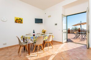 Un comedor con una mesa, sillas, un reloj, un televisor y una puerta que da a un patio exterior.
