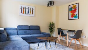 A modern living room with a sectional sofa, a round coffee table, and a dining area with a small table and chairs.