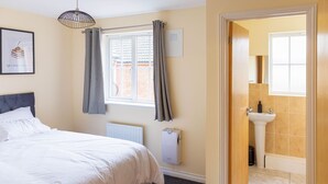 A bedroom with a bed, a radiator, a window with curtains, and a wall-mounted light fixture.