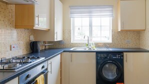 A kitchen with a stove, oven, washing machine, and a window with a view.