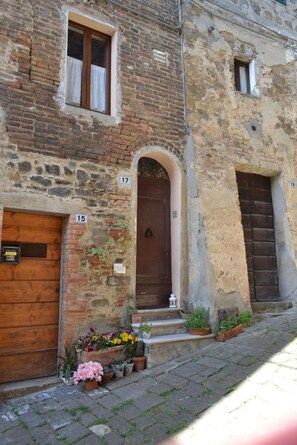 Un bâtiment historique avec des portes numérotées, une porte d’entrée en bois et des plantes en pot disposées sur les marches.