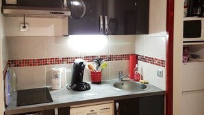 Una cocina compacta con armarios oscuros, microondas, cafetera y lavavajillas.