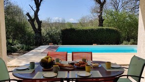 Una mesa de comedor dispuesta con platos, tazas y un frutero, con vistas a una piscina.