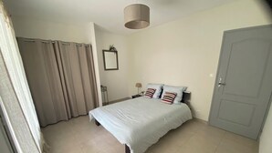 Un dormitorio con cama, cortinas, una mesita de noche, una lámpara y una puerta.