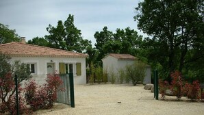 Una zona residencial privada con dos edificios blancos, un camino de grava y abundante vegetación.
