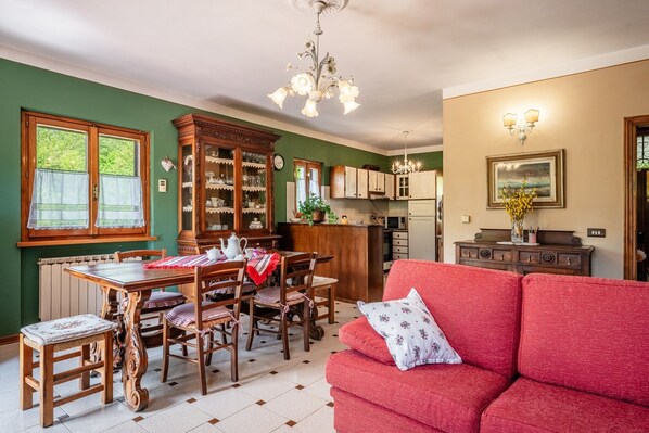 A dining area with a wooden table and chairs, a red sofa, and a kitchen in the background.