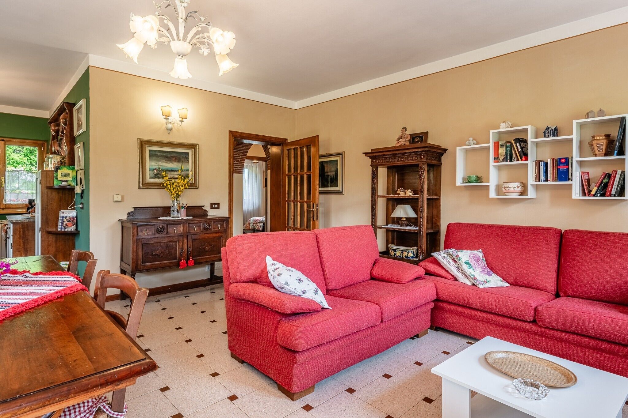 A living room with a red sofa, wooden cabinet, and a dining table with chairs.