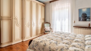 Un dormitorio con un armario grande, una cama con ropa de cama floral, una silla y un ventanal con cortinas.
