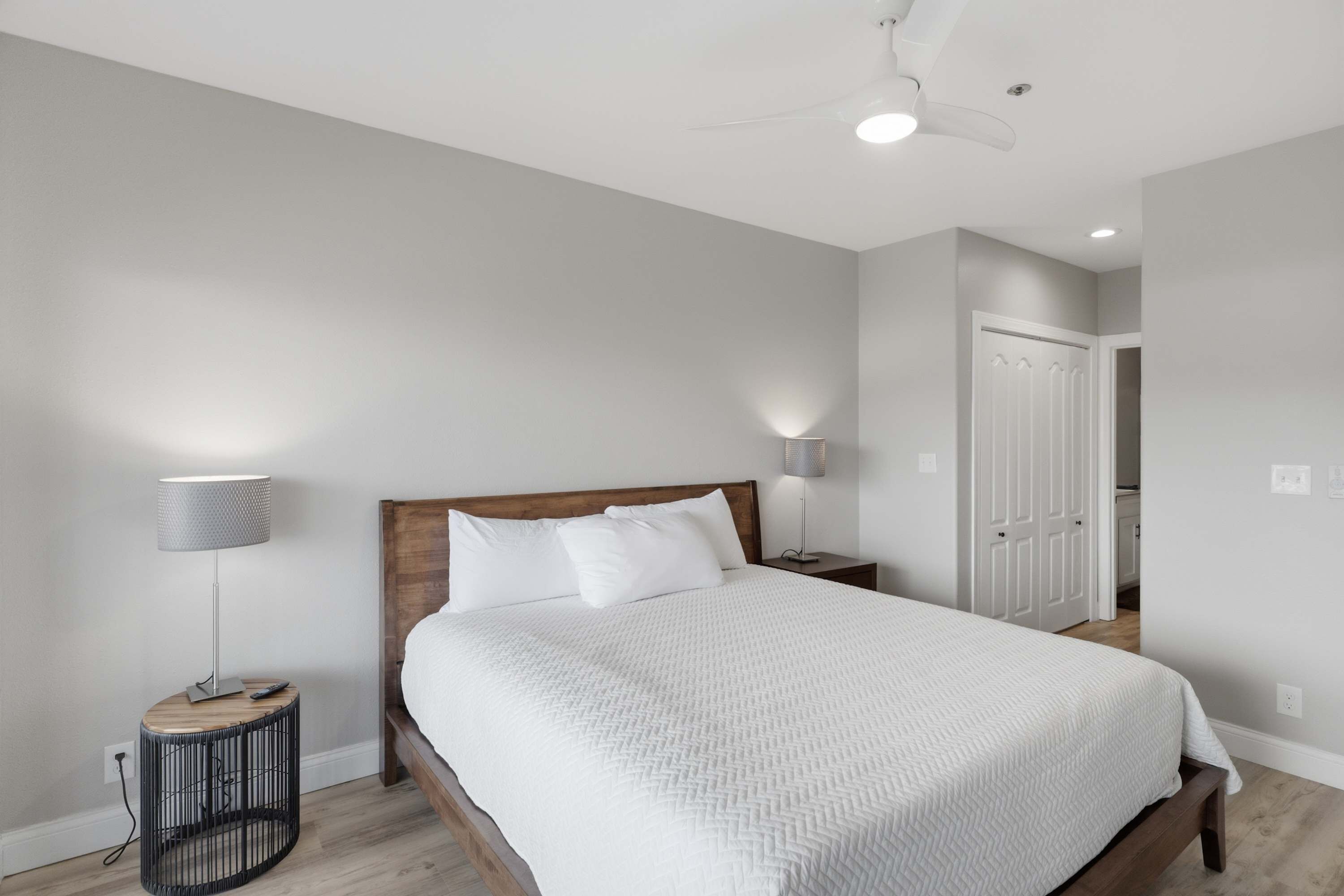 Une chambre à coucher avec un lit, des lampes de chevet, un ventilateur de plafond et une porte.