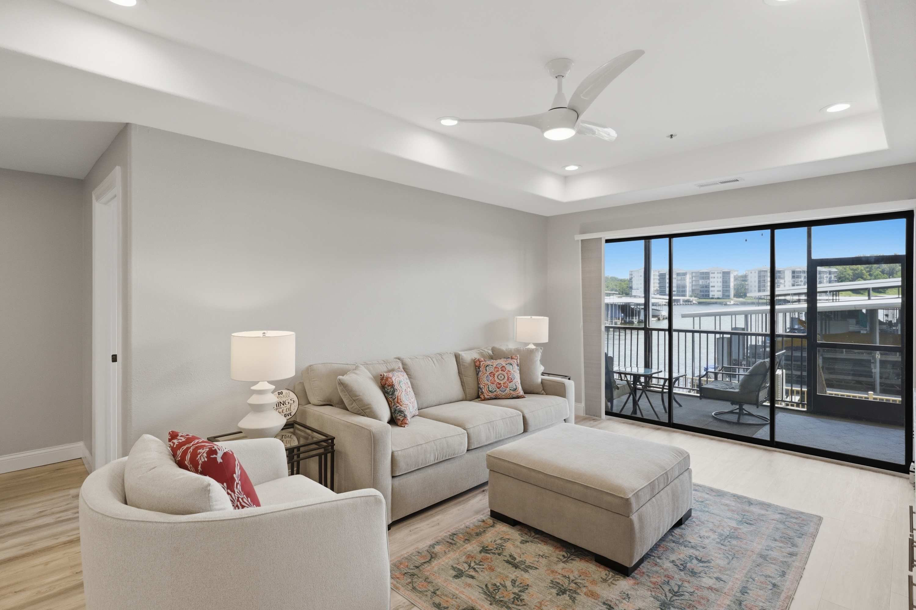 A modern living room with a sofa, ottoman, and a view of a cityscape through large windows.