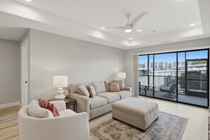 A modern living room with a sofa, ottoman, and a view of a cityscape through large windows.