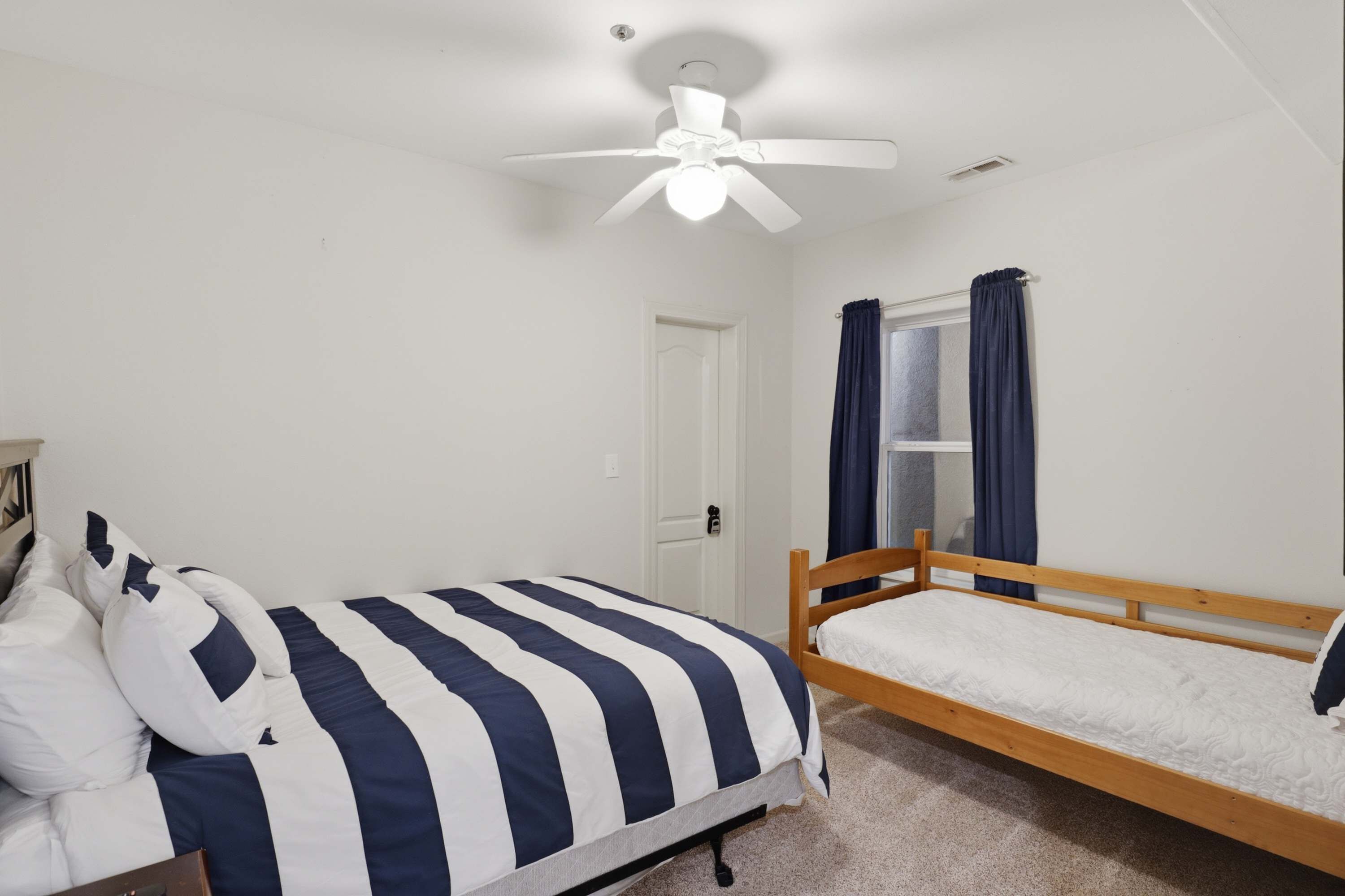 Ein Schlafzimmer mit einem Einzelbett, einem Holzkopfstück, einem Deckenventilator und einem Fenster mit Vorhängen.
