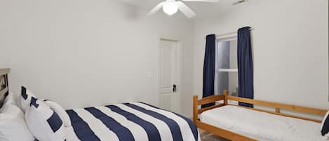 Ein Schlafzimmer mit einem Einzelbett, einem Holzkopfstück, einem Deckenventilator und einem Fenster mit Vorhängen.