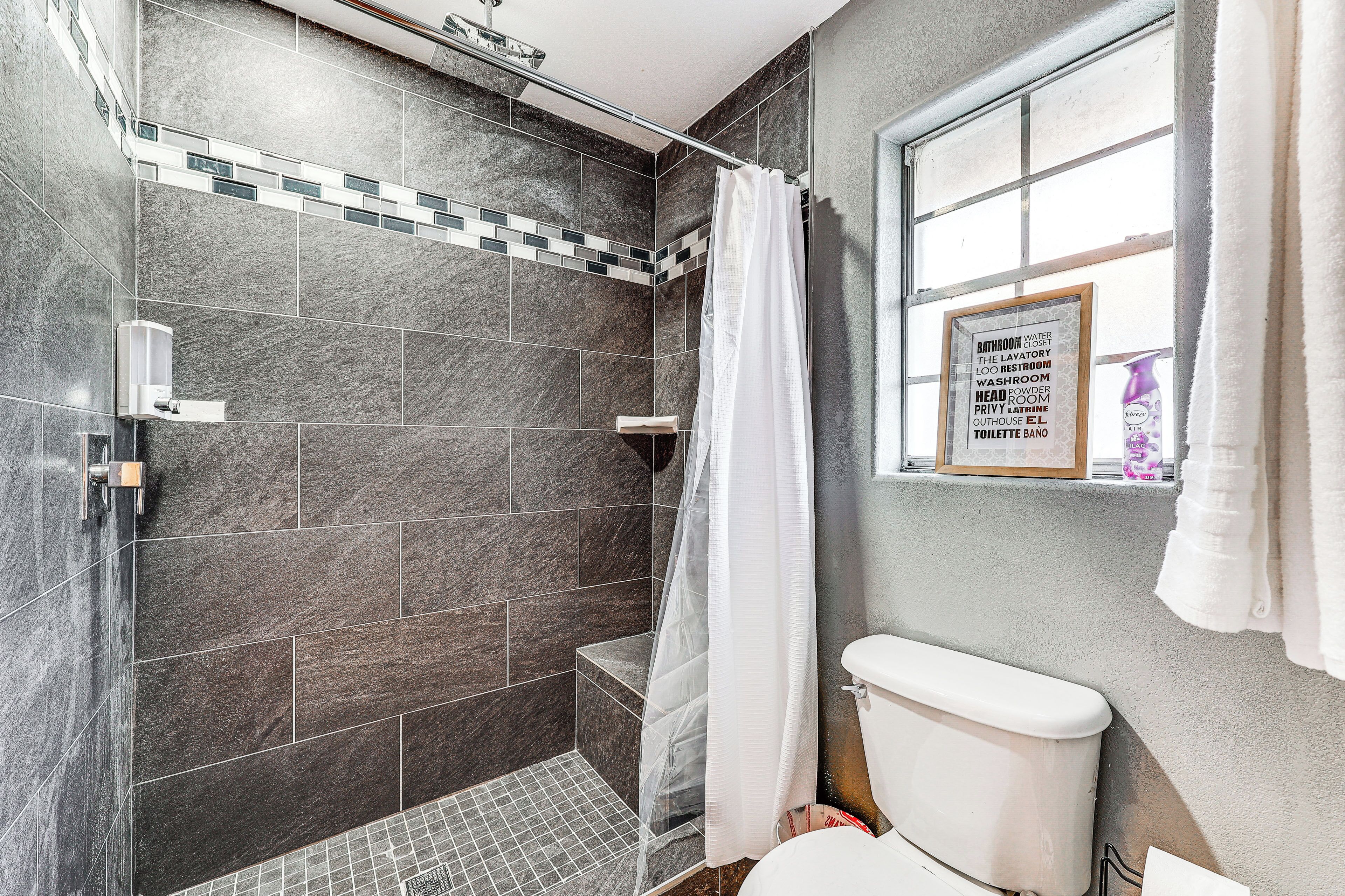 Un bagno moderno con piastrelle scure, cabina doccia in vetro e un cartello incorniciato che elenca i servizi.