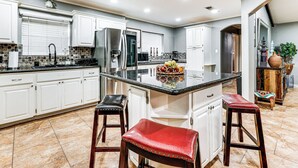 A modern kitchen with white cabinets, a central island with stools, and a large refrigerator. - 3 Mi to Downtown Mcallen: Quiet Home w/ Pool (McAllen)