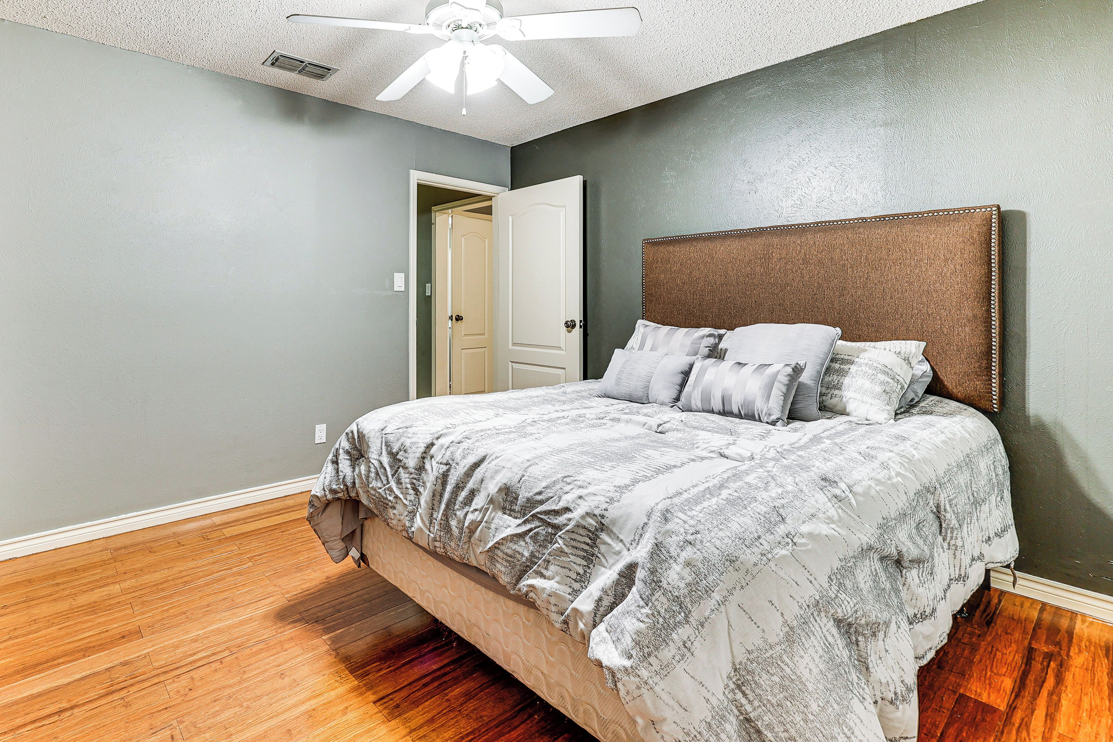 A bedroom with a bed, a ceiling fan, and a door leading to another room.